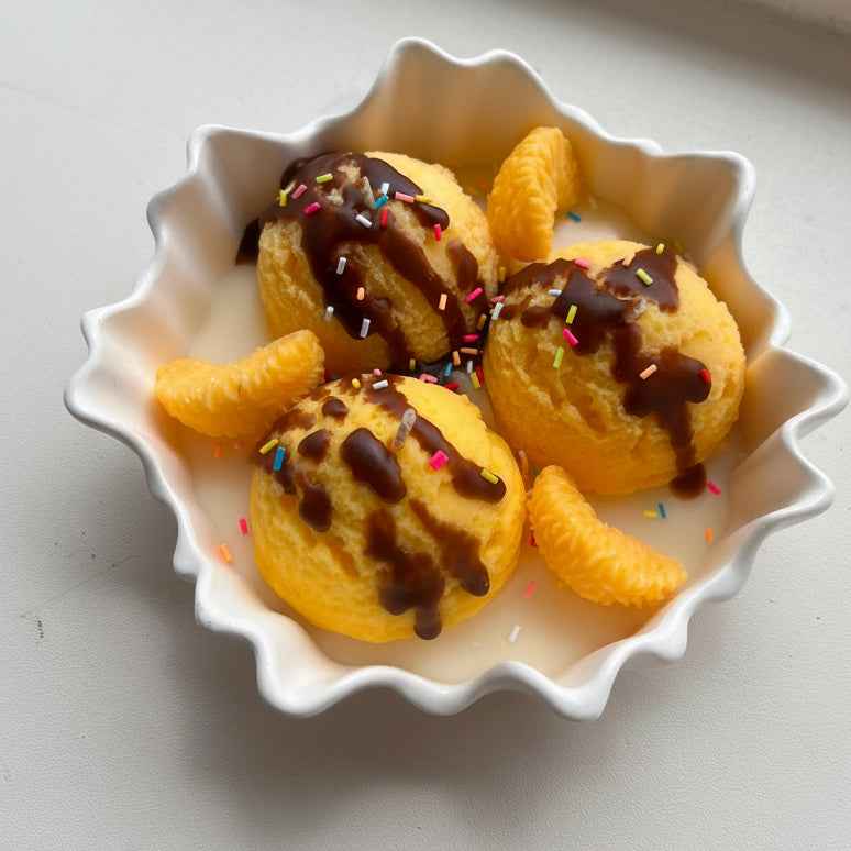 Dessertkaars met bollen van was, chocoladesaus en sprinkles in een geschulpte keramieken coupe