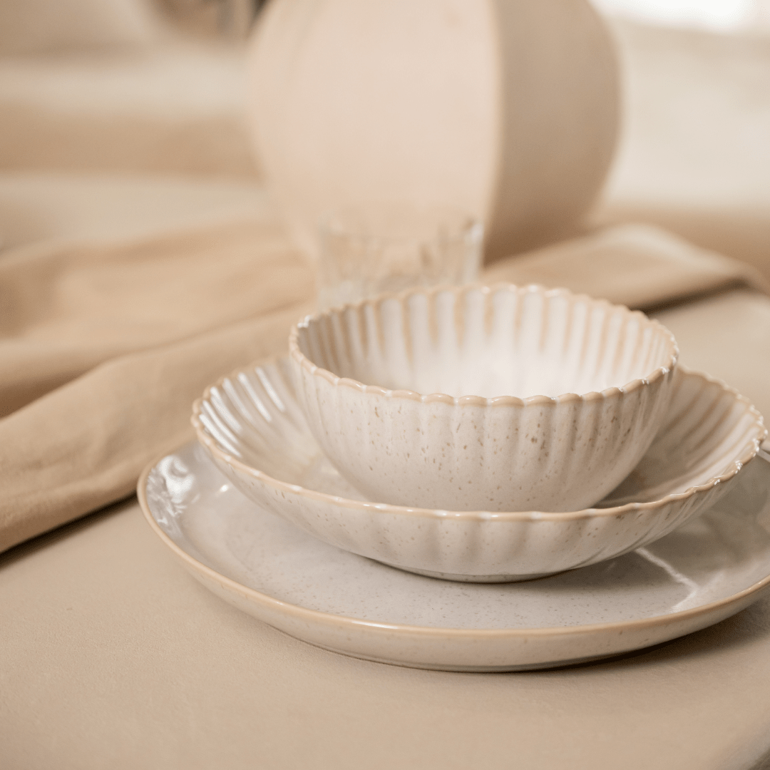 Gestapeld gebroken wit servies met een linnen servet op een lichte tafel.
