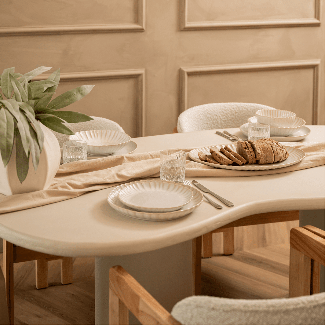 Gedekte tafel met gebroken wit servies, brood en salie bij een panelen wand.