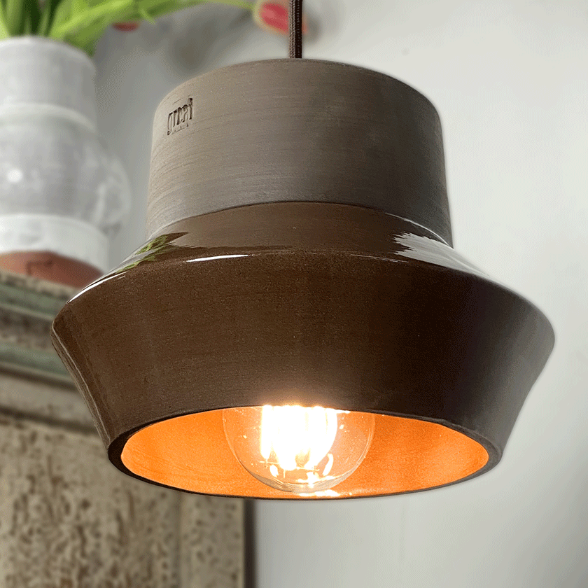 Brede keramieken hanglamp met chocoladebruin glazuur en brandende lamp.