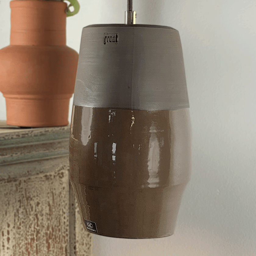 Keramieken hanglamp met chocoladebruin glazuur boven een verweerde kast.