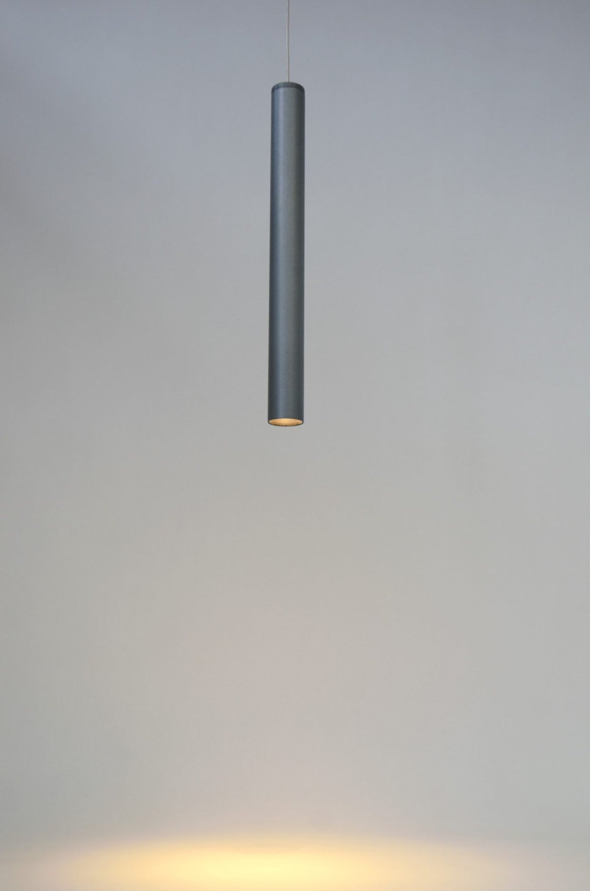 Titaankleurige cilindrische hanglamp die een smalle bundel licht naar beneden geeft.
