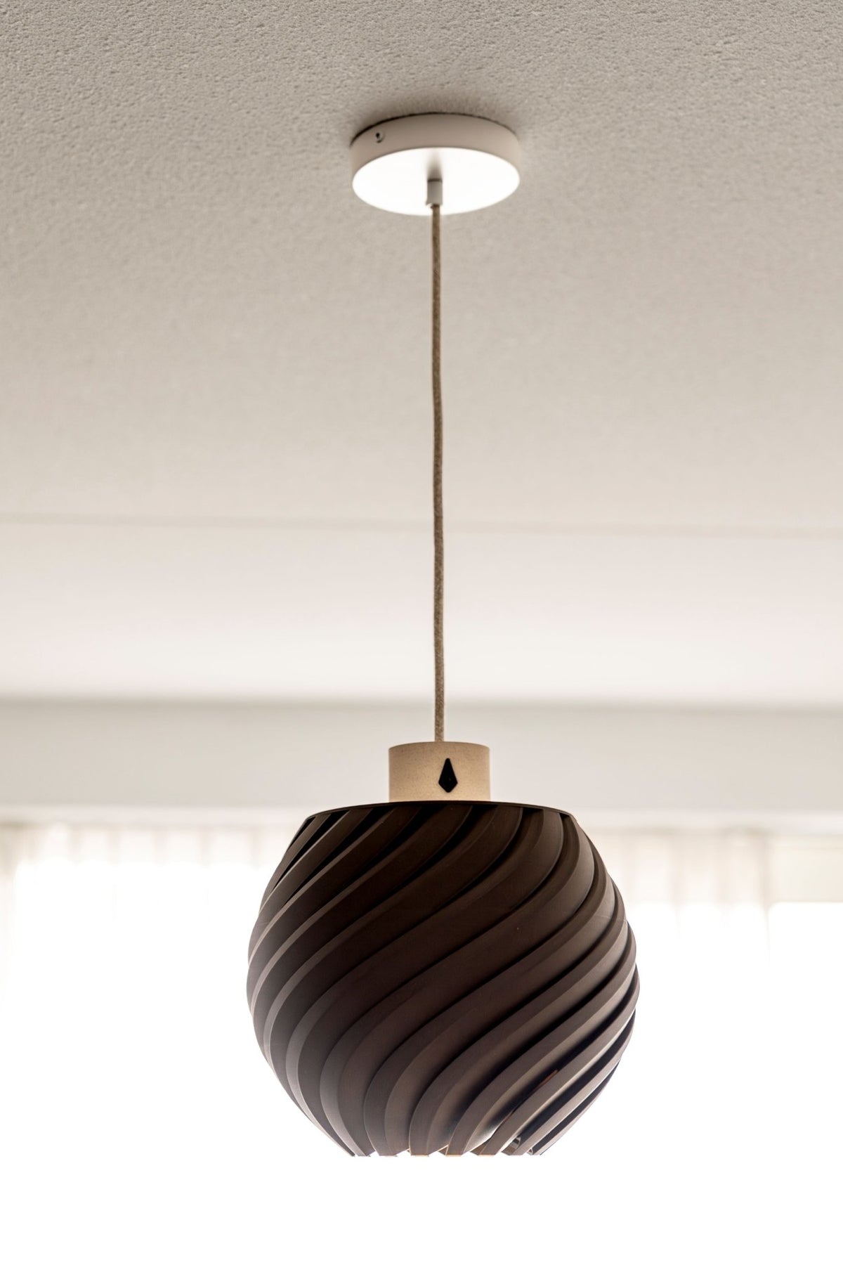 Donkerbruine bolvormige hanglamp met golvend reliëf aan een snoer onder een wit plafond.