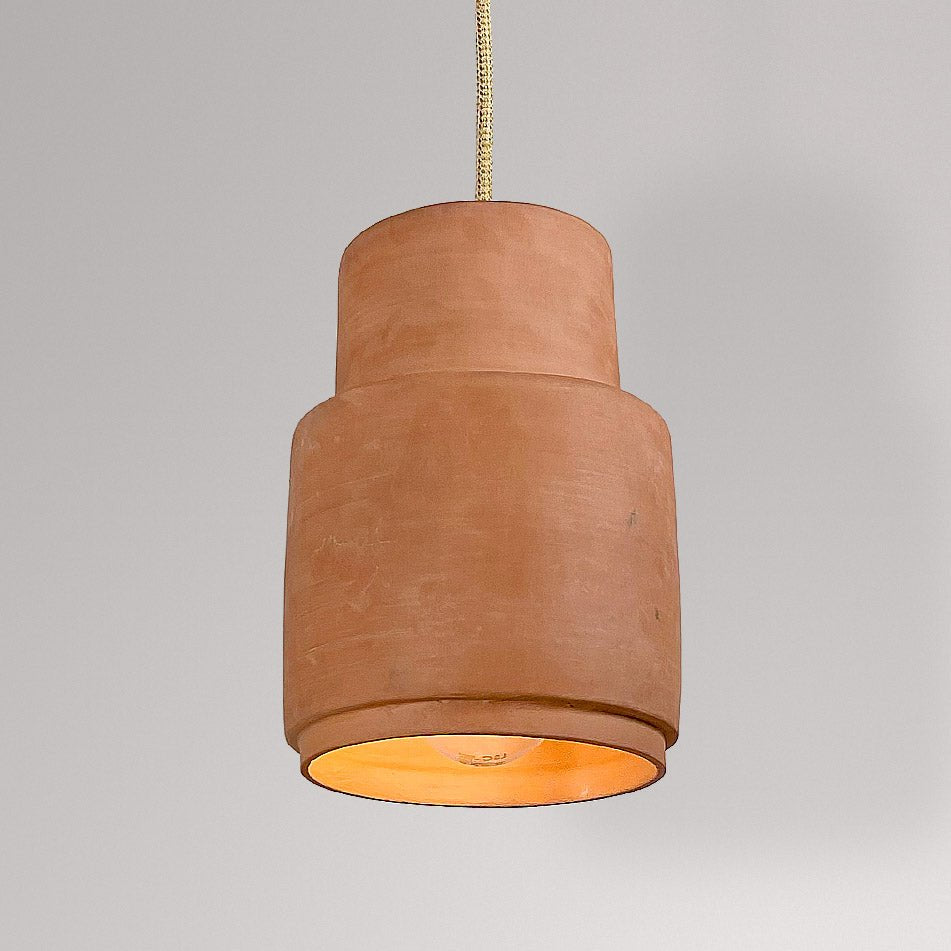 Gelaagde cilindrische keramieken hanglamp in terracotta met brandende lamp.