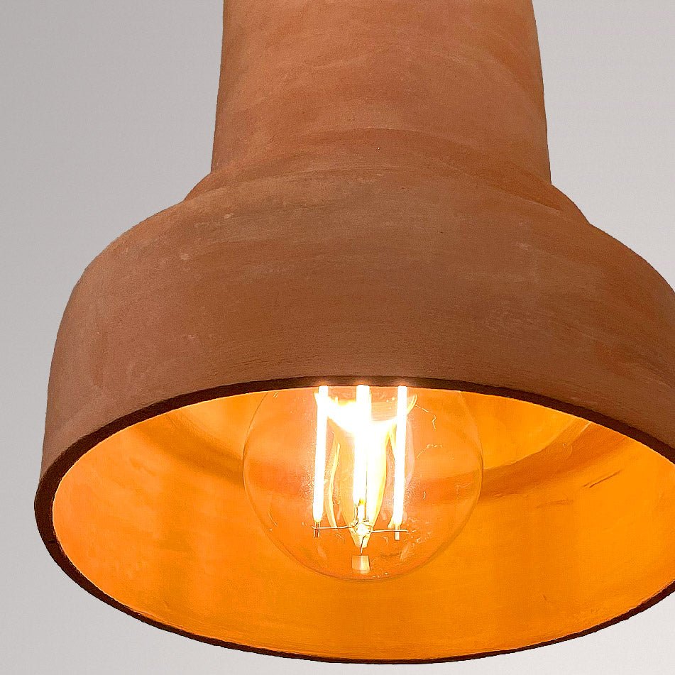 Onderaanzicht van een terracotta keramieken hanglamp met brandende lamp.