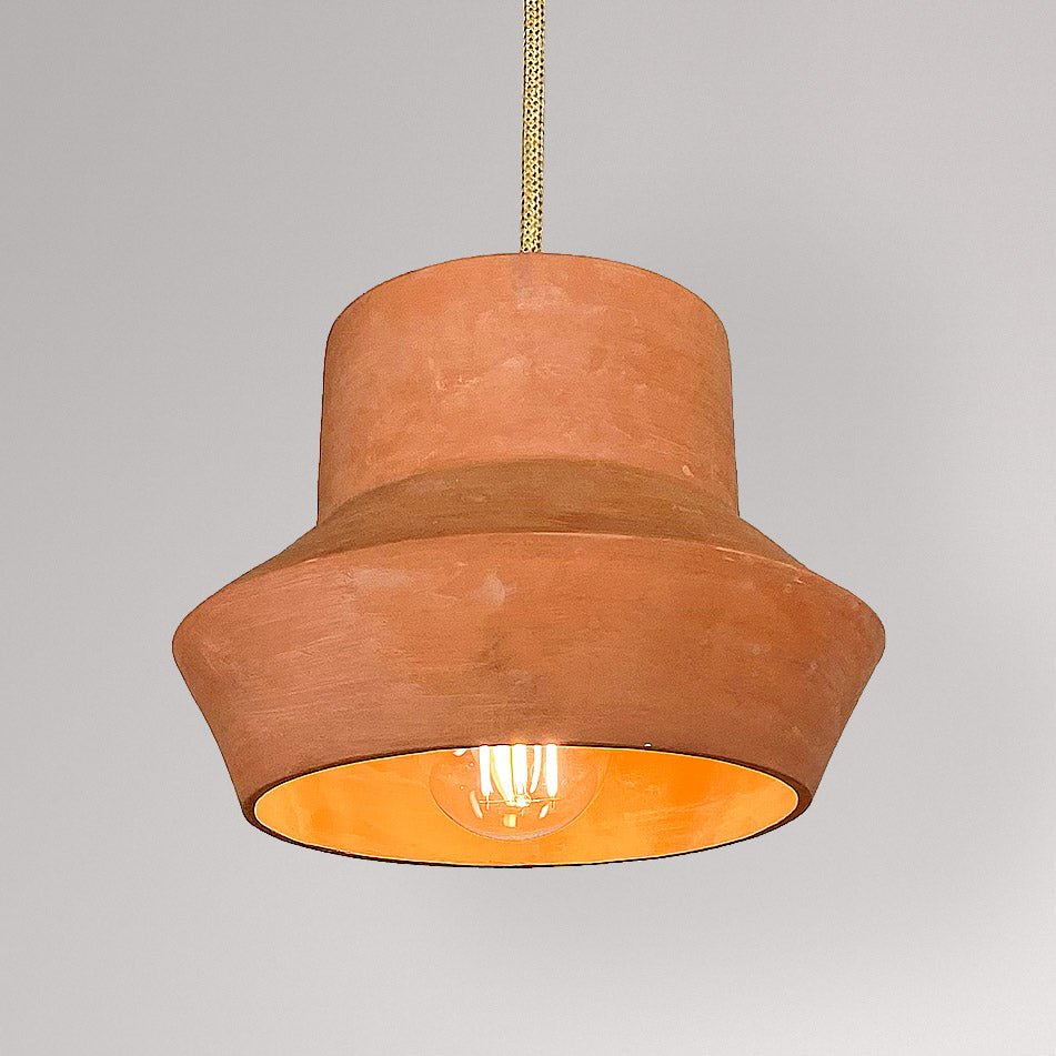 Brede, lage keramieken hanglamp in terracotta met brandende lamp en warm oplichtende binnenzijde.