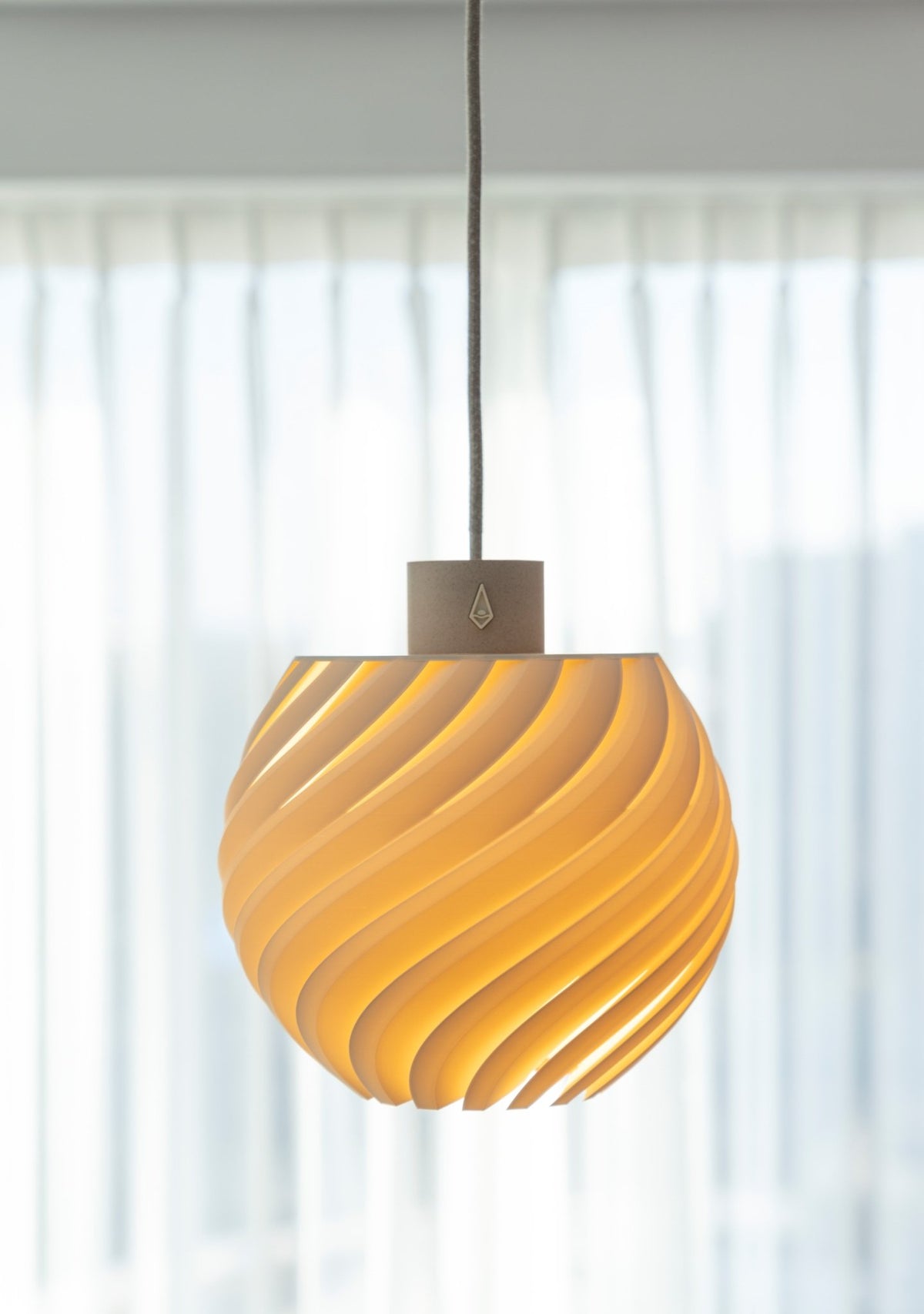 Bolvormige hanglamp met golvend reliëf en warm brandend licht voor een raam met wit gordijn.