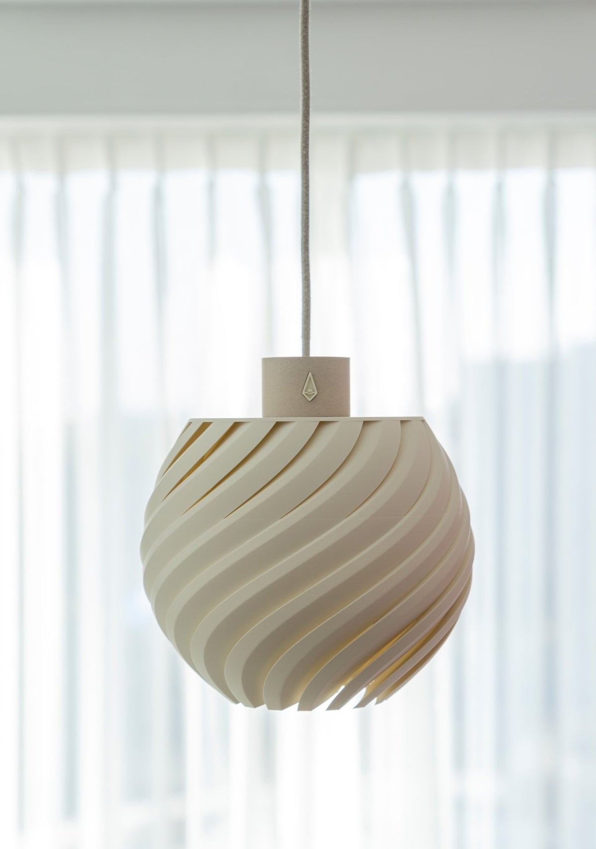 Gebroken witte bolvormige hanglamp met golvend reliëf aan een snoer voor een licht raam.