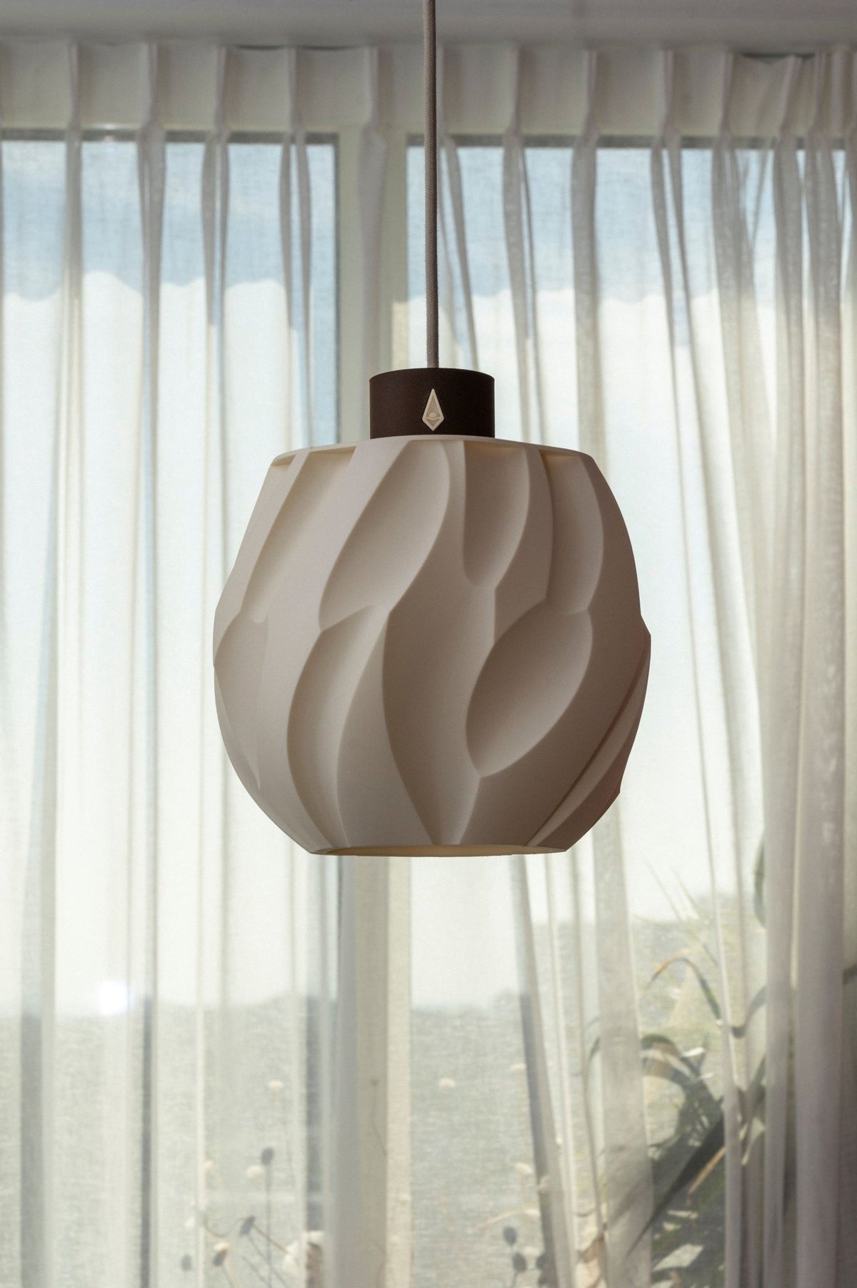 Gebroken witte bolvormige hanglamp met diep zandreliëf aan een snoer voor een licht raam.