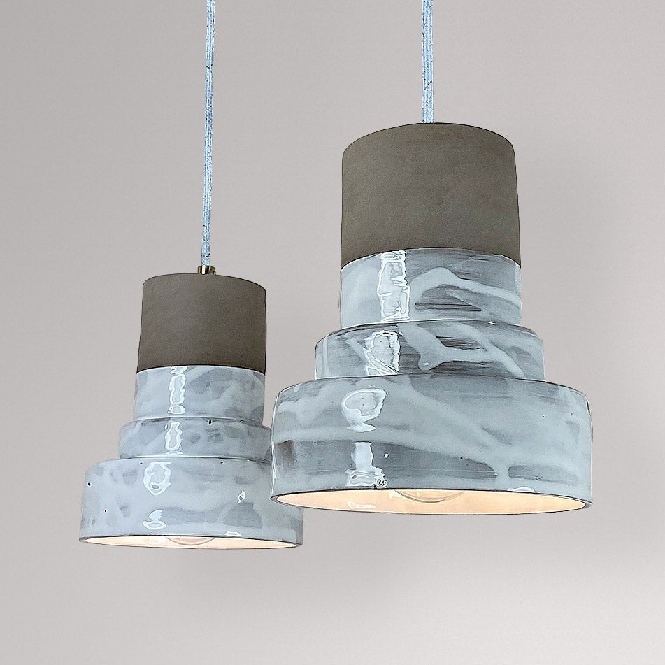 Twee getrapte keramieken hanglampen met wit gemarmerd glazuur en licht aan.