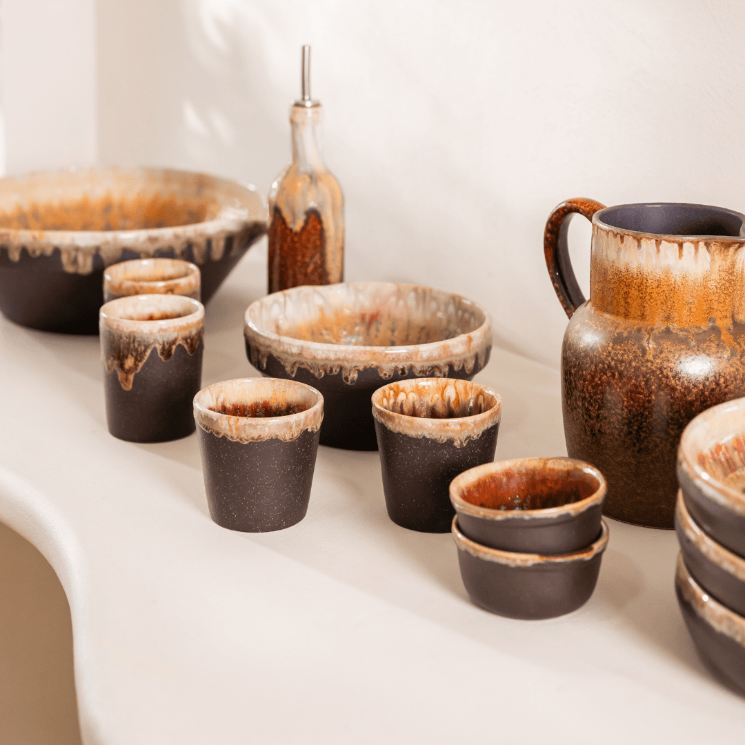 Servies in donkerbruin keramiek met druipglazuur, opgesteld op een lichte tafel.