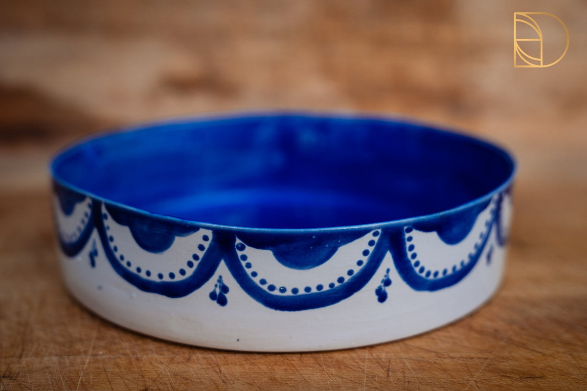Ronde keramieken schaal met kobaltblauwe binnenzijde en wit met blauw geschilderd slingermotief.