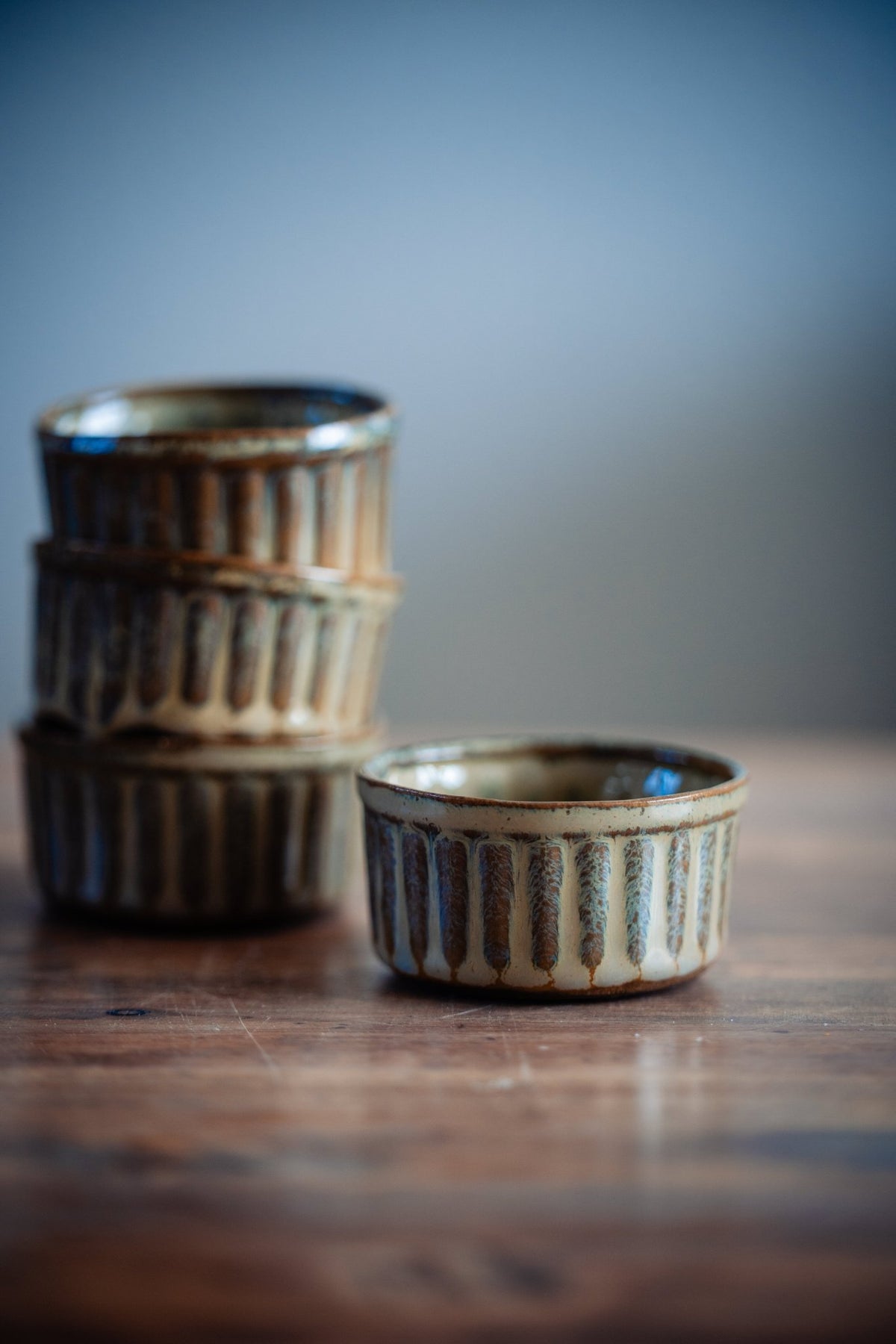 Twee geribbelde keramieken schaaltjes naast een stapel op een houten tafel.