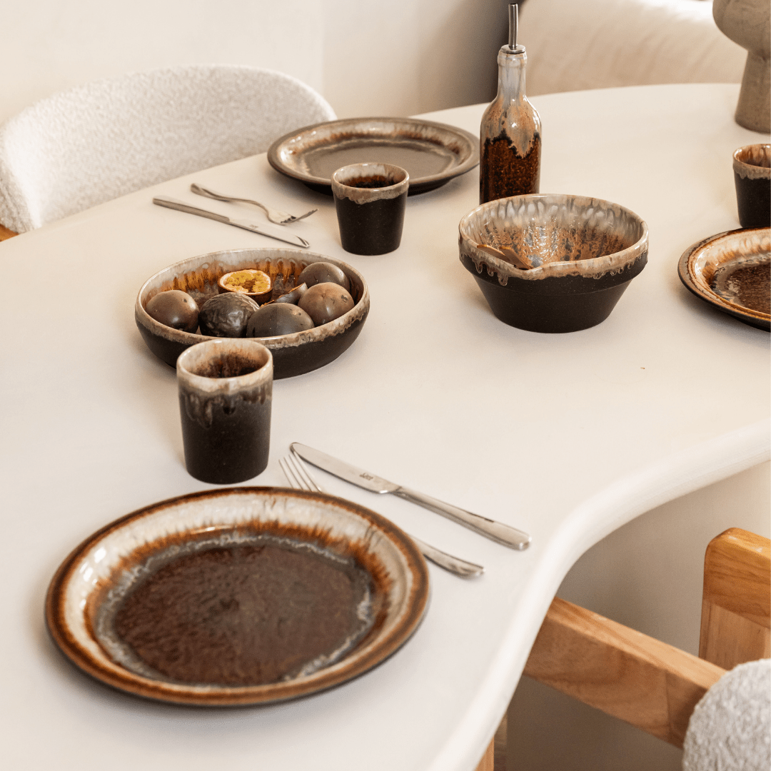 Gedekte tafel met donkerbruin servies, bestek en een schaal met noten.