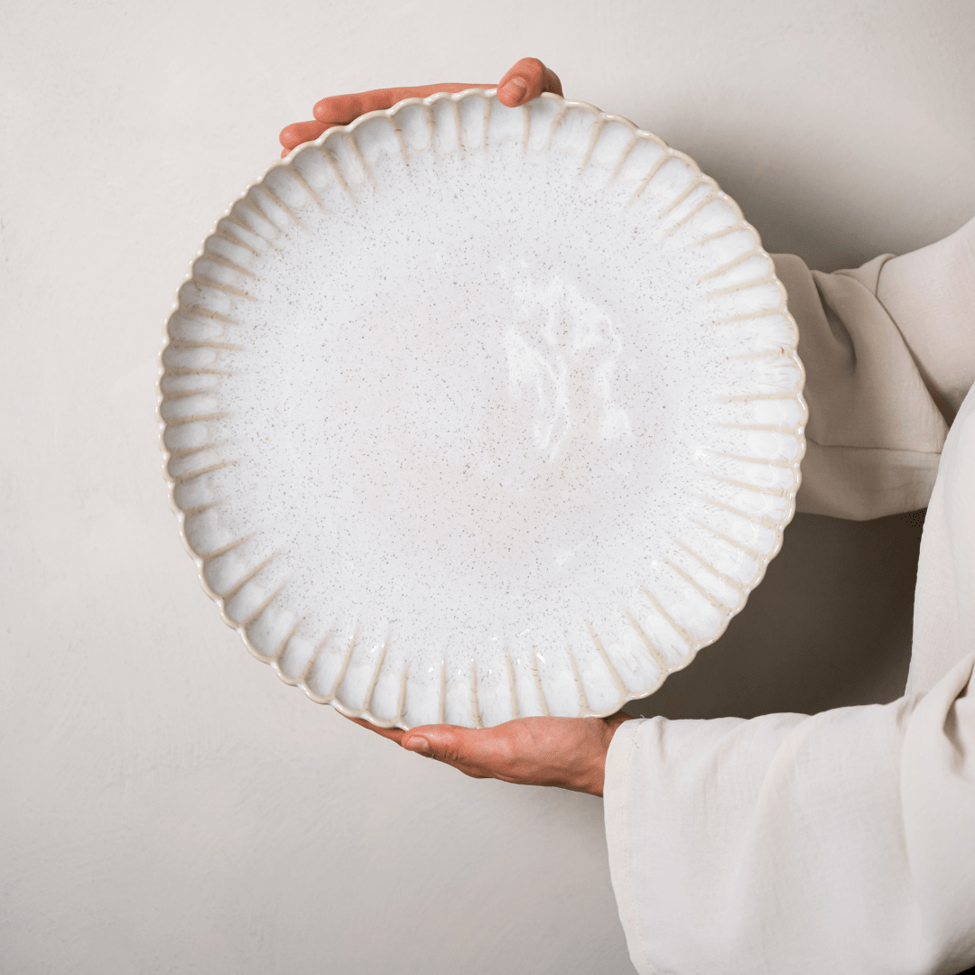 Grote ronde gebroken witte schaal met geschulpte rand, met twee handen vastgehouden.