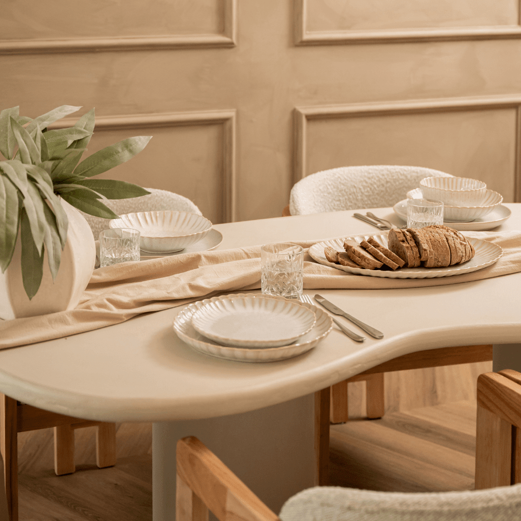 Gedekte tafel met gebroken wit servies, glazen en een tak salie in een vaas.