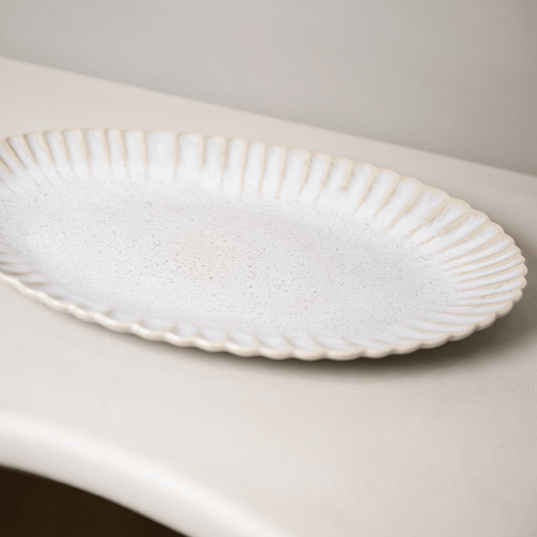 Ovale gebroken witte serveerschaal met geschulpte rand op een lichte tafel.