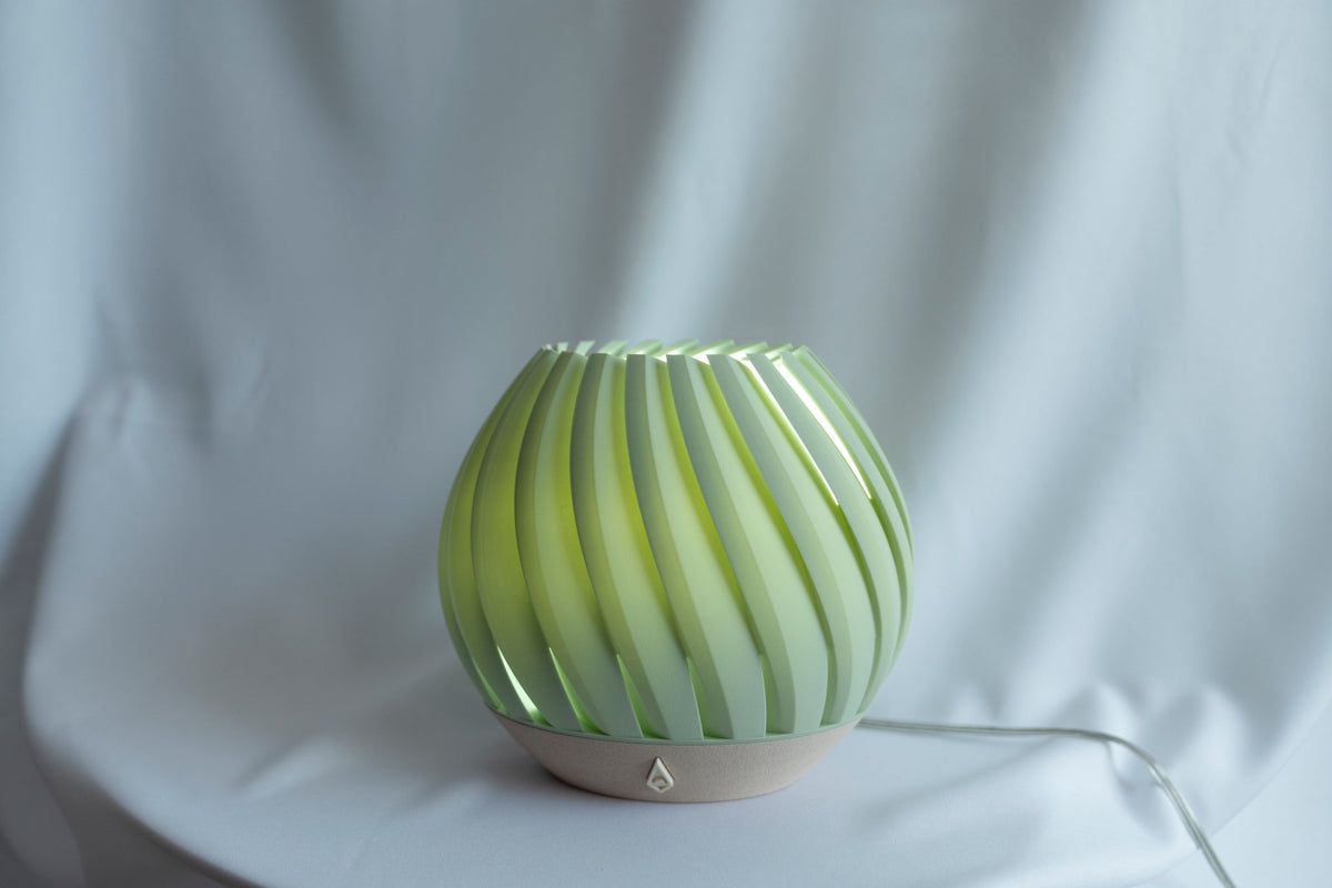 Frisgroene brede tafellamp met geribbelde schelpvorm tegen een witte doek in daglicht.