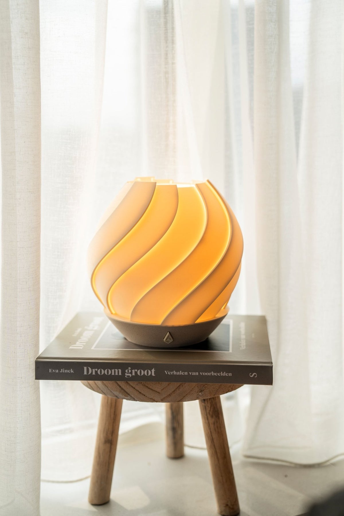 Bolvormige tafellamp met zeewierreliëf en warm brandend licht op een houten krukje.