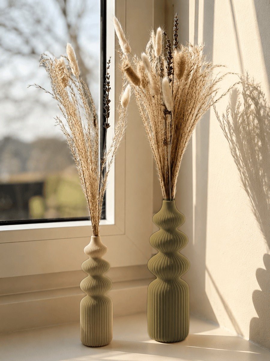 Twee vazen met bolvormige geledingen in goud, met droogbloemen bij een raam.