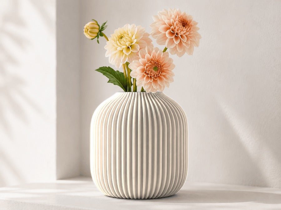 Geribbelde vaas in mat wit met dahlia's erin, voor een lichte muur.