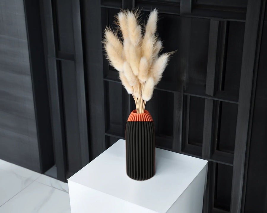 Slanke geribbelde vaas in mat zwart met droogbloemen erin.