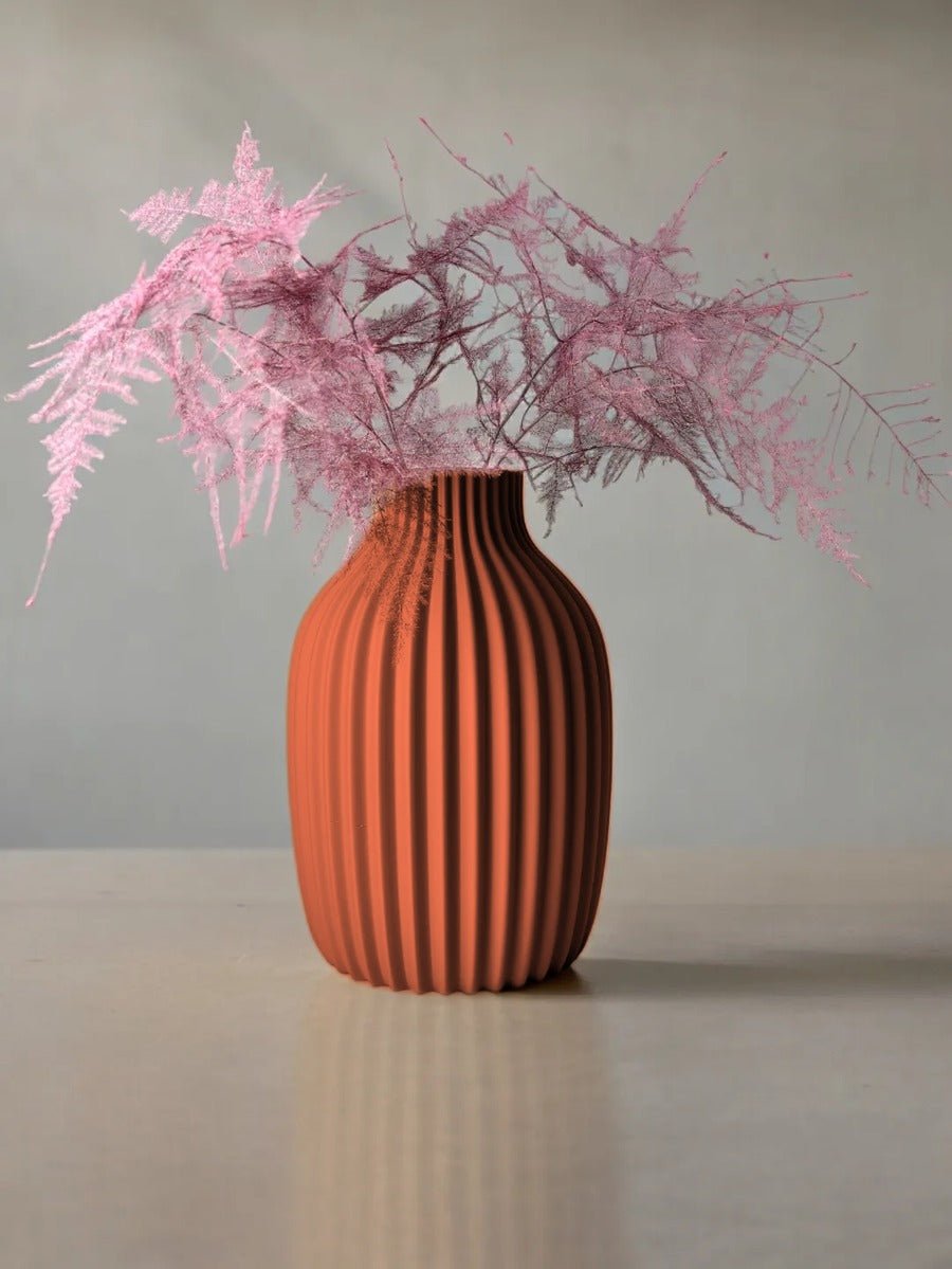 Vaas met verticale rimpelribbels in terracotta, met roze droogtakken erin.