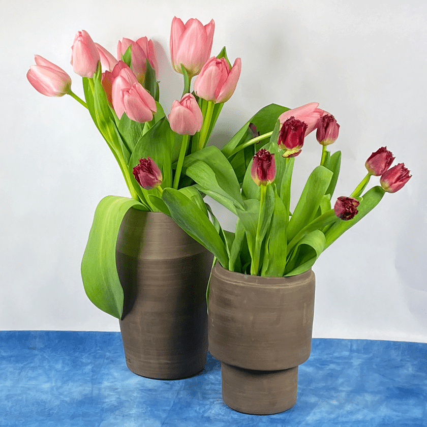 Twee chocoladebruine keramieken vazen met roze en rode tulpen.