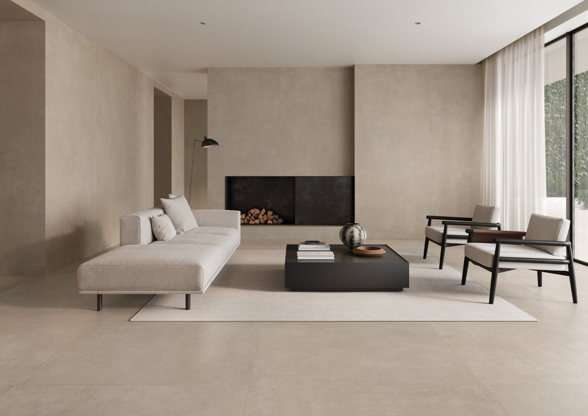 Woonkamer met grijsbeige betonlook vloer, witte hoekbank, zwarte haard en houten fauteuils.