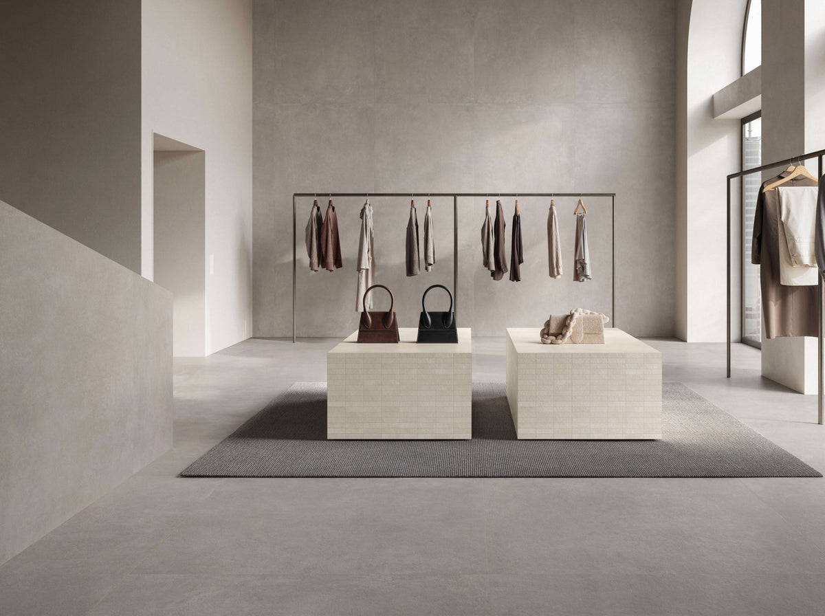 Winkelruimte met grijze betonlook vloer, kledingrek en lage presentatietafels.