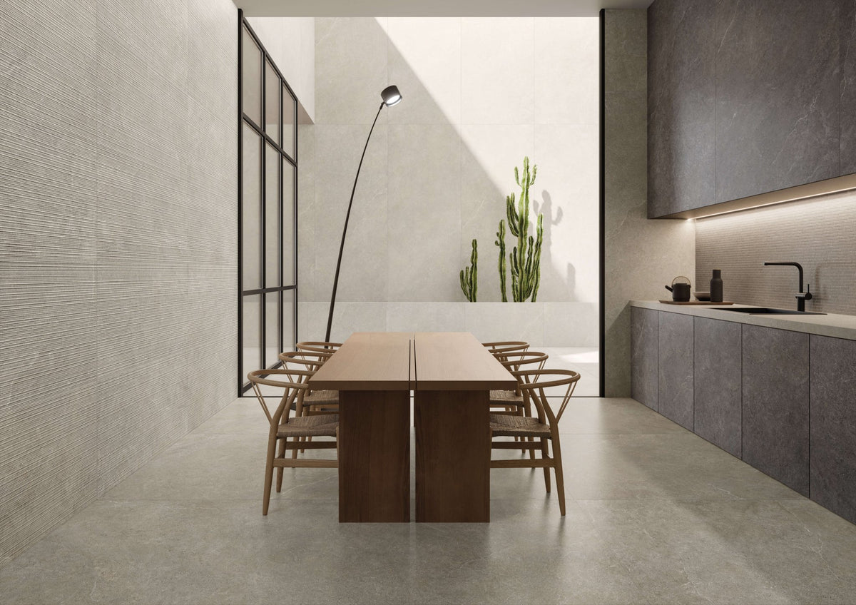 Eethoek met taupe kalksteenlook vloer, houten tafel, rieten stoelen en een keuken op de achtergrond.