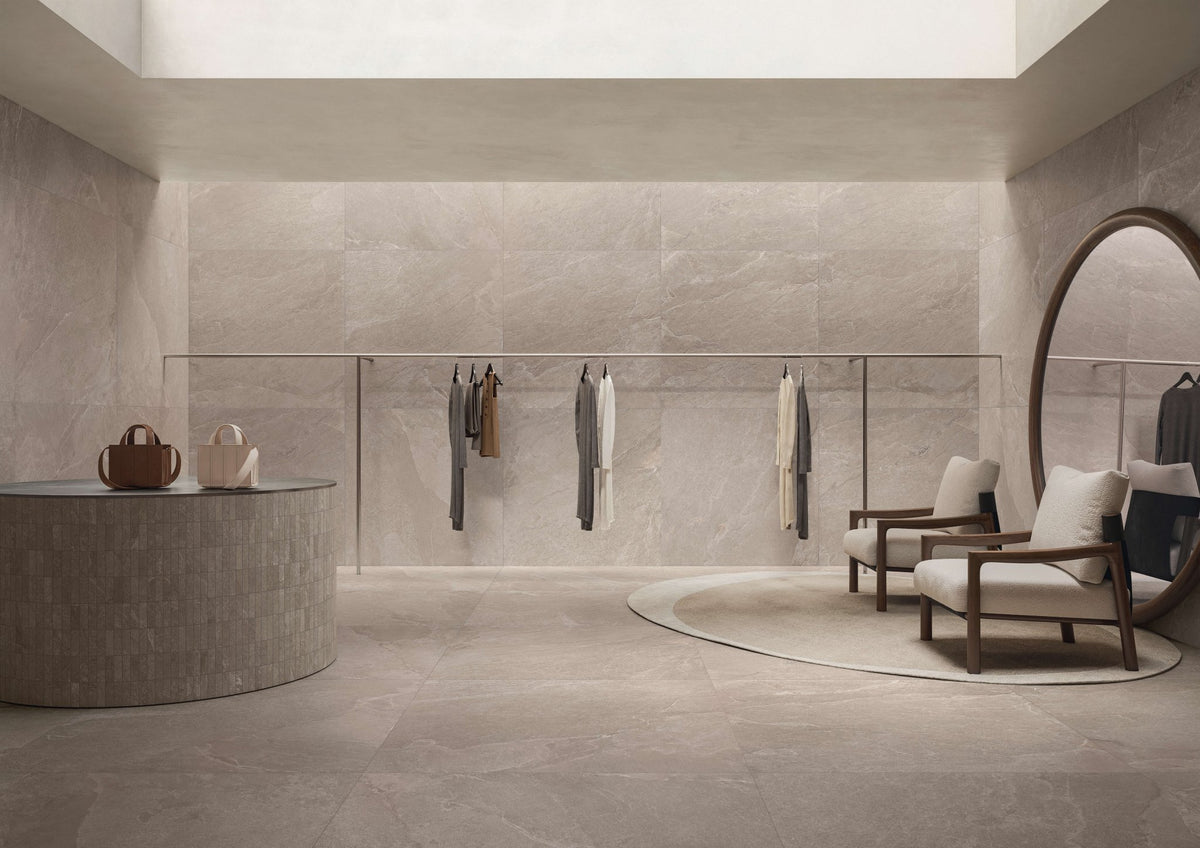 Winkelinterieur met taupe leisteenlook vloer, ronde balie, kledingrekken en een ronde spiegel.