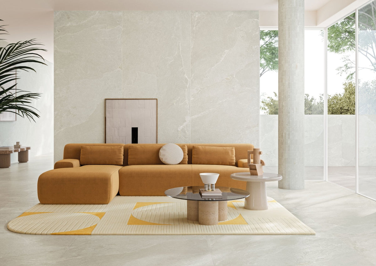 Woonkamer met lichte leisteenlook vloer, oranje bank en een geel vloerkleed.