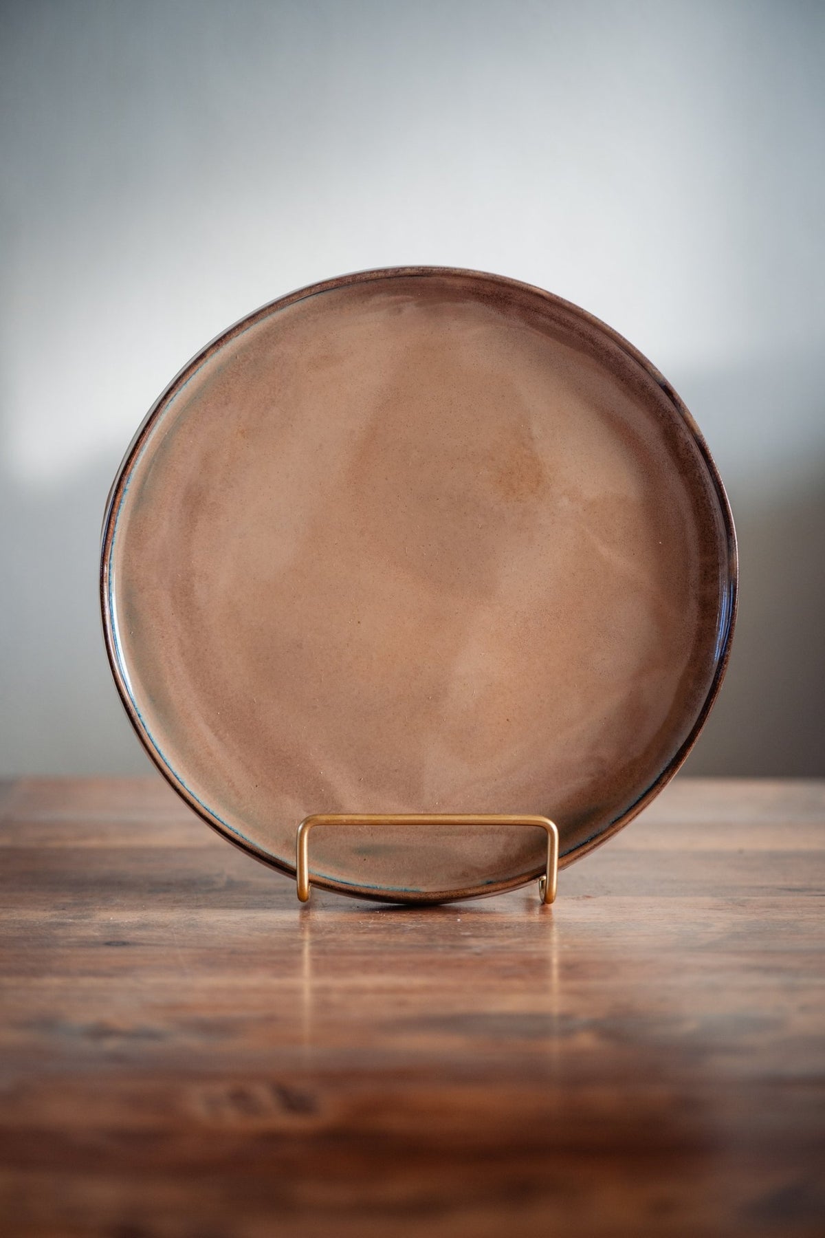 Keramieken dinerbord met rozebeige reactief glazuur en donkere rand op een standaard.