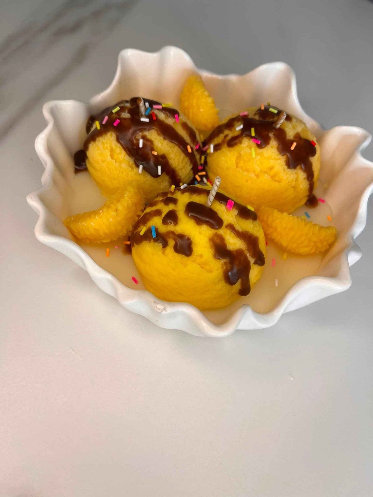 Waxbollen in geel met chocoladesaus en gekleurde sprinkles in een witte geschulpte coupe
