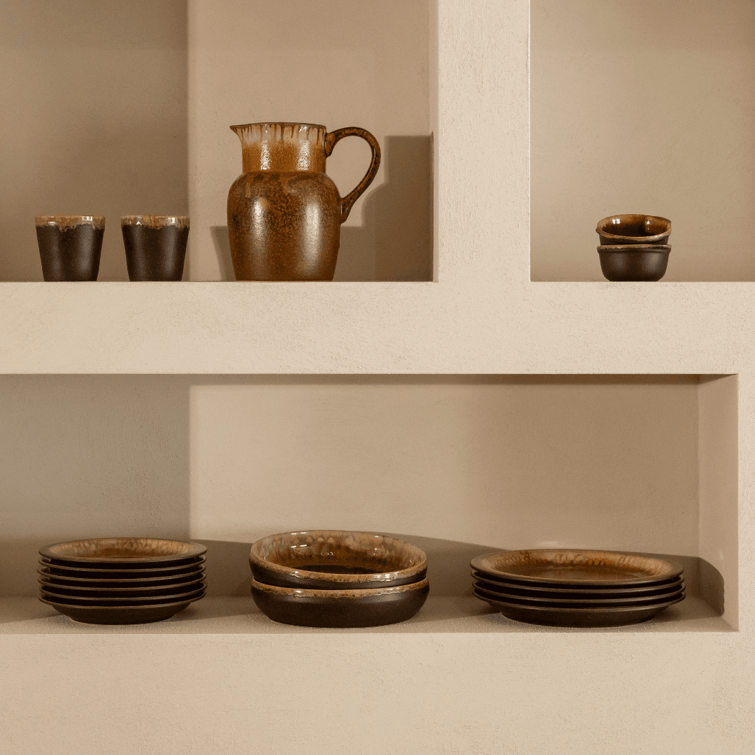 Donkerbruin servies in wandnissen, met een kan, bekers en een schaaltje.