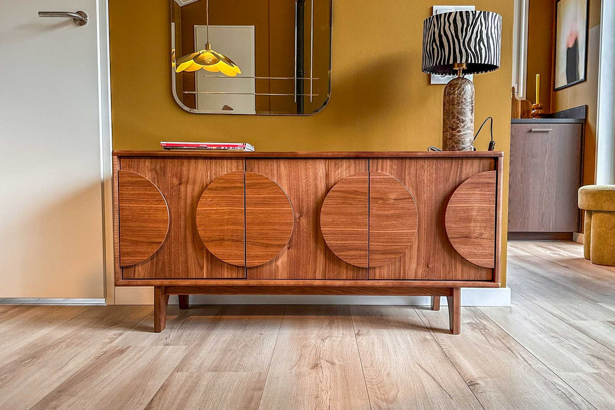 Notenhouten dressoir met ronde accenten op de deuren, tegen een okergele wand in een hal