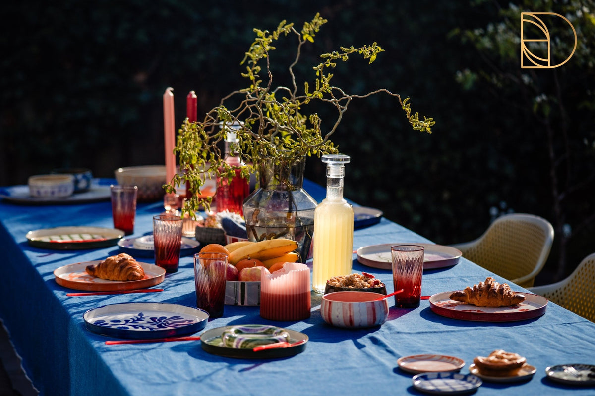 Gedekte tafel buiten met blauw kleed, kaarsen en handbeschilderd keramiek.