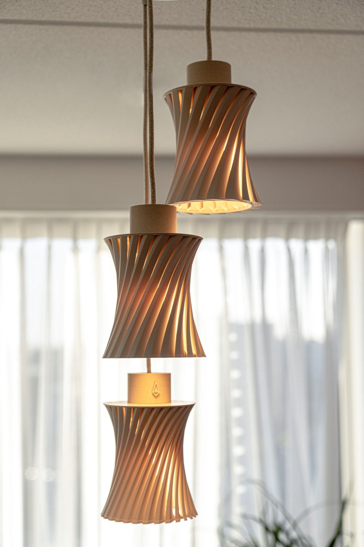 Drie zandbeige geribbelde lampenkappen met brandend warm licht dat tussen de spiraalribbels door schijnt.