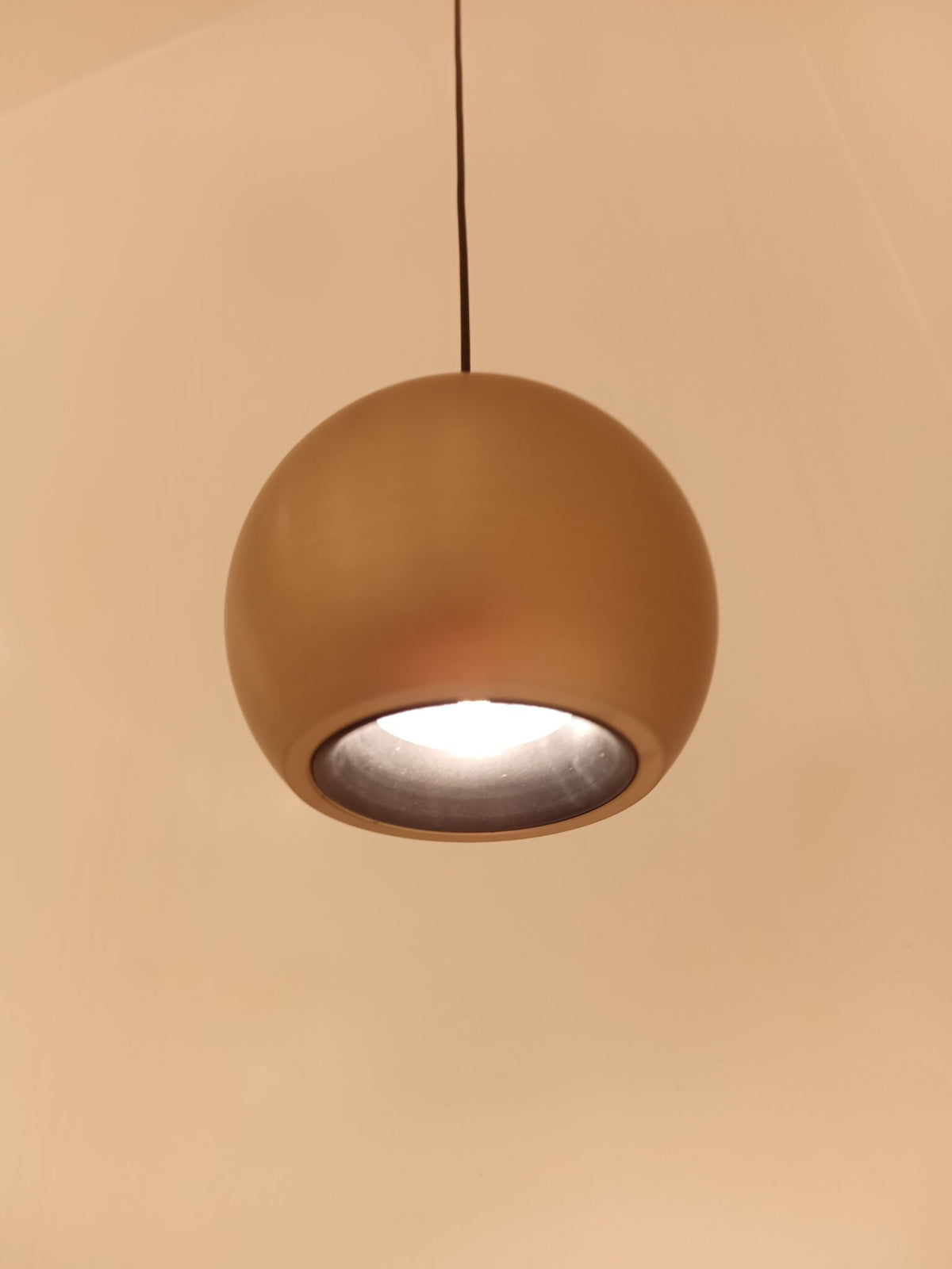 Champagnekleurige bolvormige hanglamp die brandt en warm licht naar beneden geeft.
