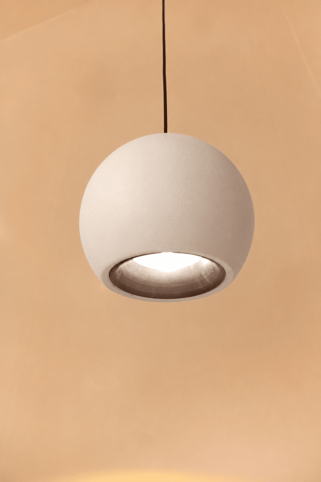 Witte bolvormige hanglamp die brandt boven een warme achtergrond.