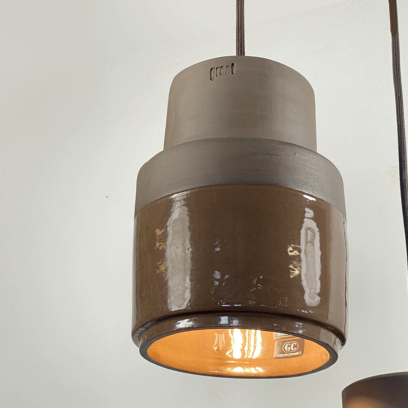 Cilindrische keramieken hanglamp met chocoladebruin glazuur en brandende lamp.