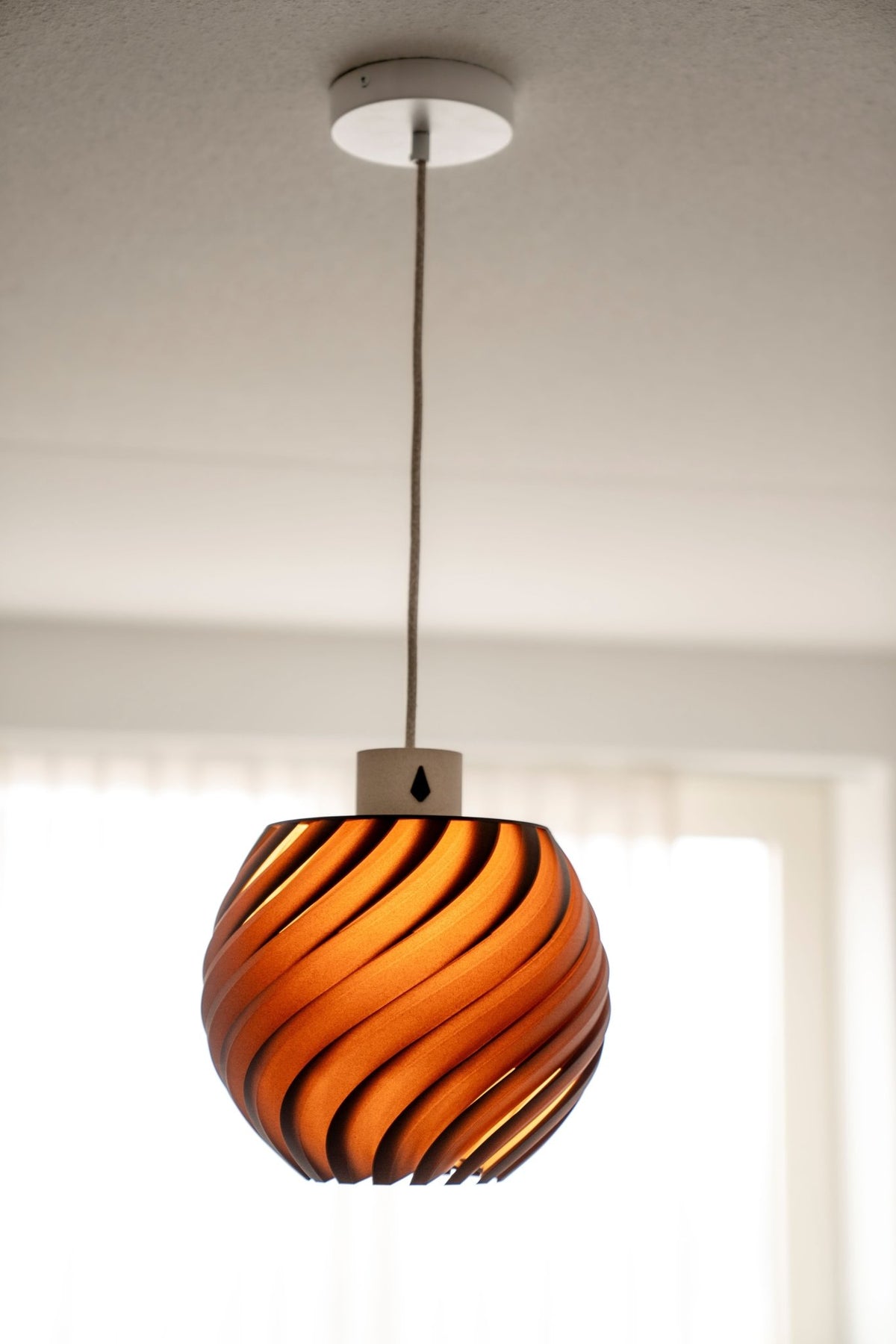 Donkerbruine bolvormige hanglamp met warm brandend licht dat tussen het reliëf door schijnt.