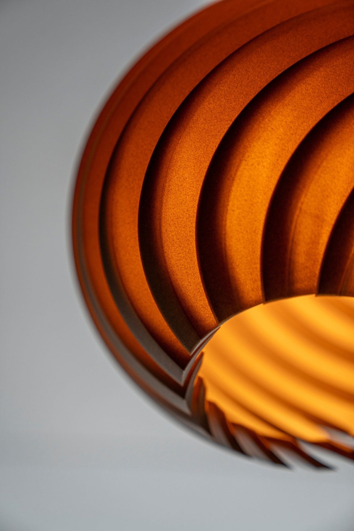 Detail van een brandende bolvormige lampenkap waarin het golfreliëf oranje oplicht.