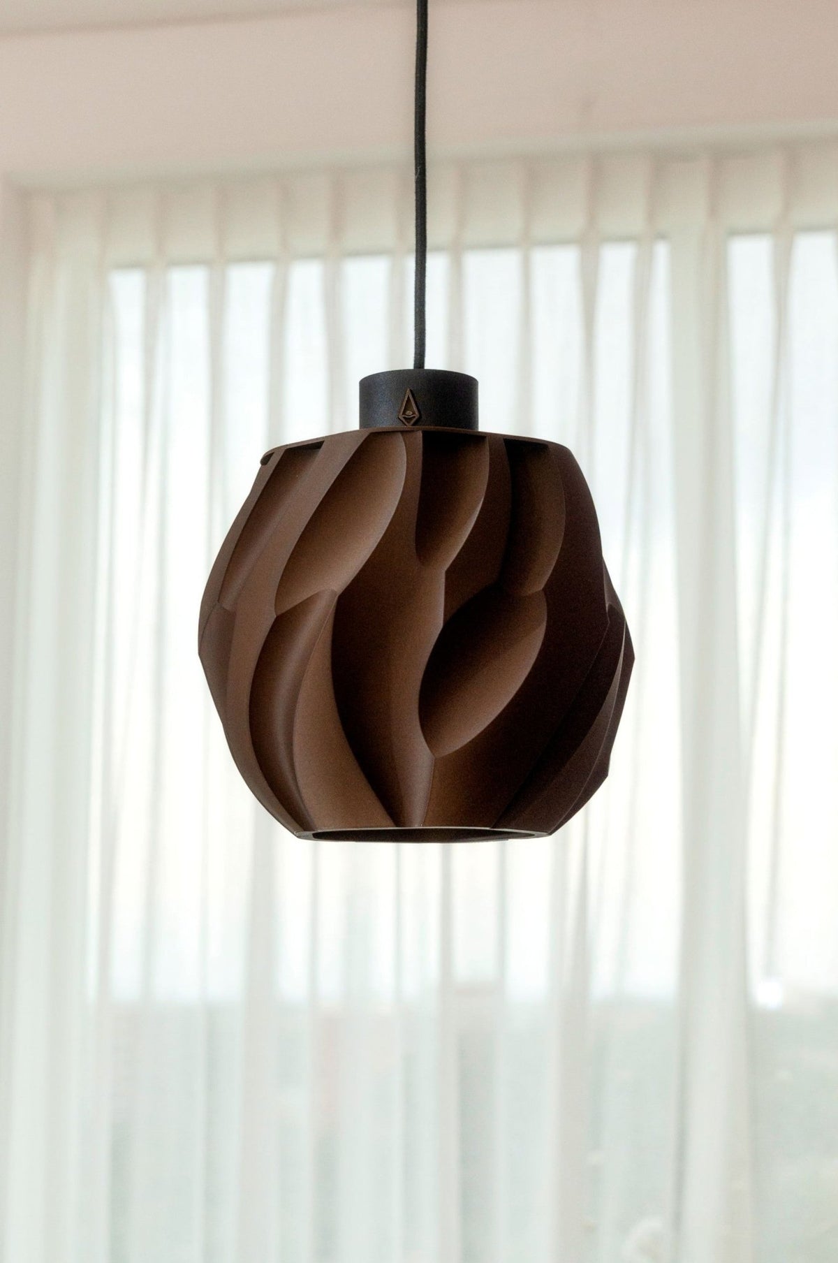 Donkerbruine bolvormige hanglamp met diep zandreliëf aan een snoer voor een licht raam.