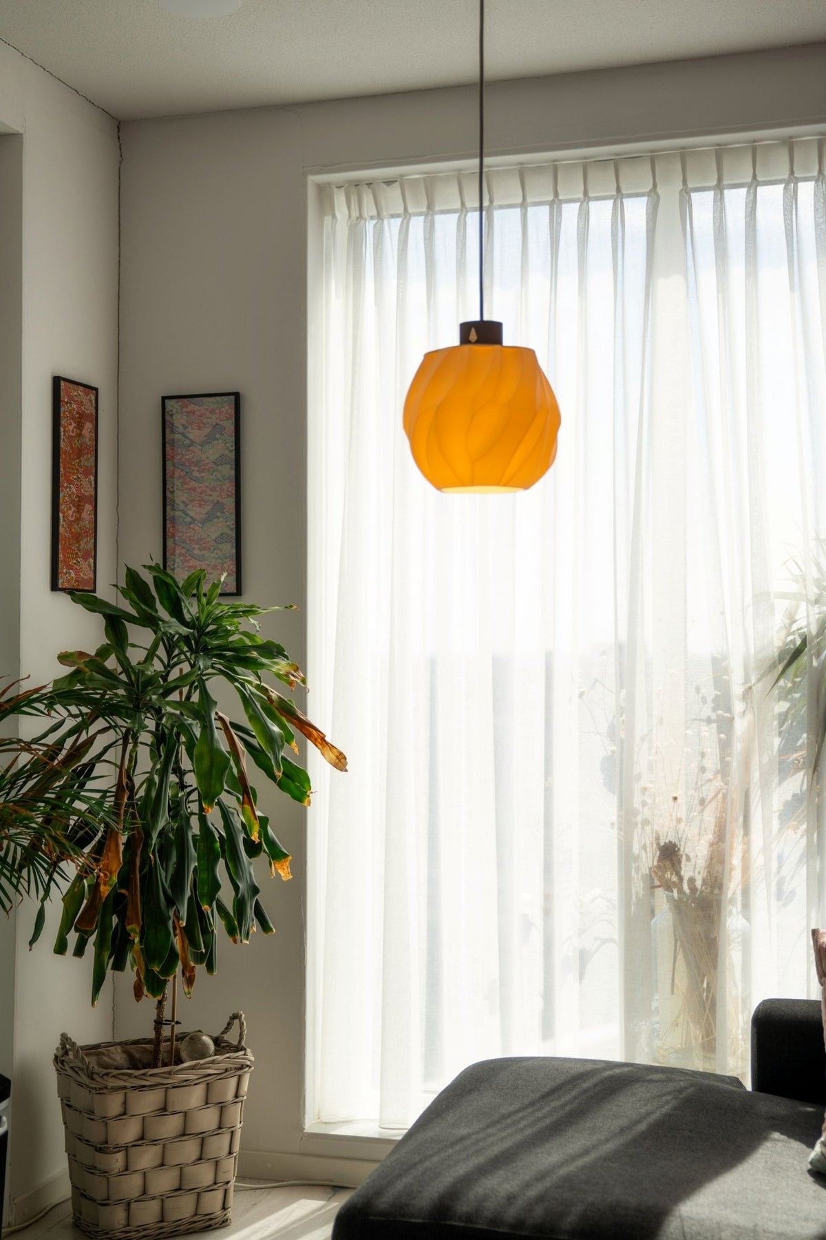 Brandende bolvormige hanglamp in een lichte woonkamer met een plant in een mand en een bank.