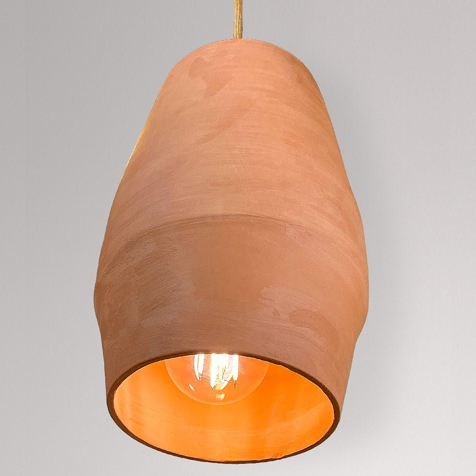 Langgerekte keramieken hanglamp in terracotta met brandende lamp.