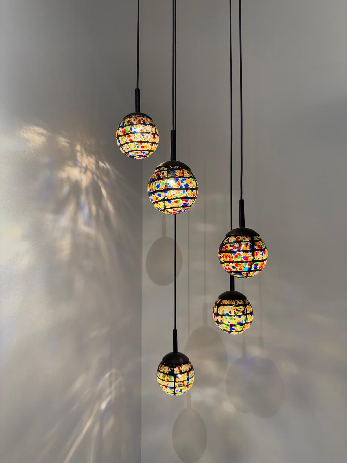 Hanglamp met vijf kleine bollen van kleurrijk kunstglas aan zwarte snoeren.