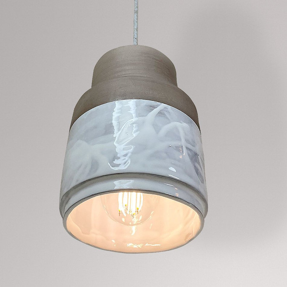 Cilindrische keramieken hanglamp met wit gemarmerd glazuur en brandende lamp.