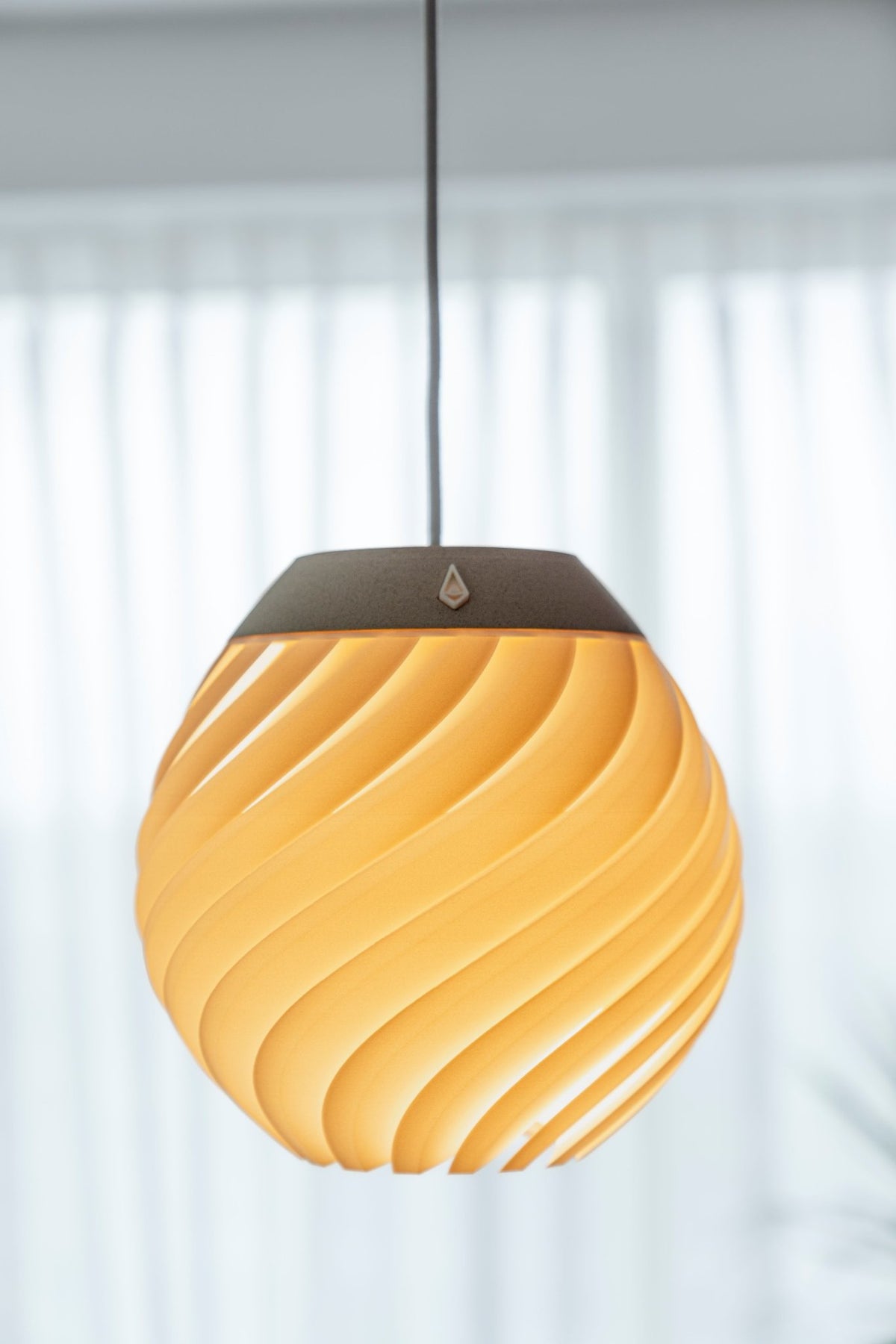 Bolvormige hanglamp met dicht golfreliëf en warm brandend licht voor een raam met wit gordijn.